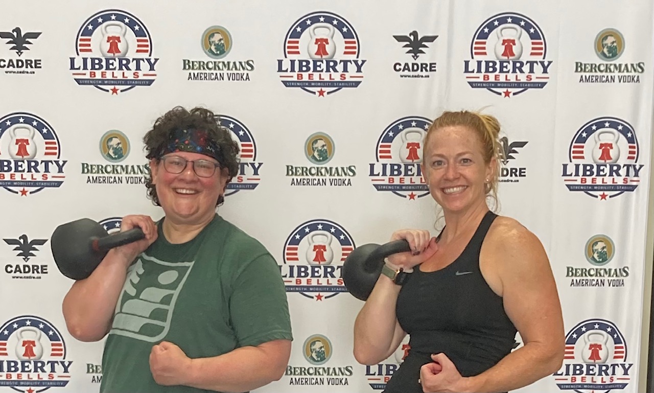 Two smiling Liberty Bells members racking kettlebells at the gym in Leander, TX
